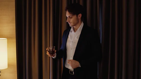 Selbstbewusster Geschäftsmann hält Glas Whiskey im Hotelzimmer — Stockfoto