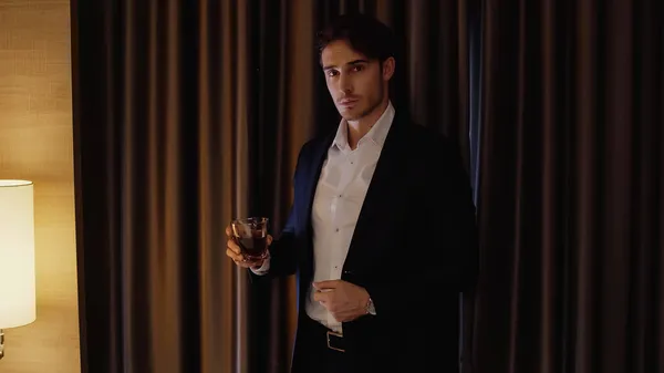 Homme d'affaires confiant tenant un verre de whisky dans la chambre d'hôtel — Photo de stock