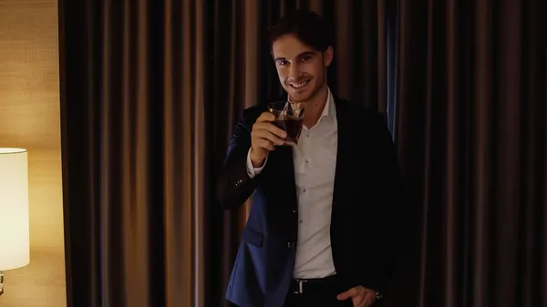 Happy businessman holding glass of whiskey in hotel room — Stock Photo