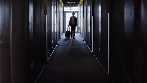 Hombre de negocios con maleta caminando por el pasillo del hotel - foto de stock