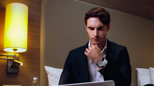 Thoughtful young businessman using laptop in hotel room — Stock Photo