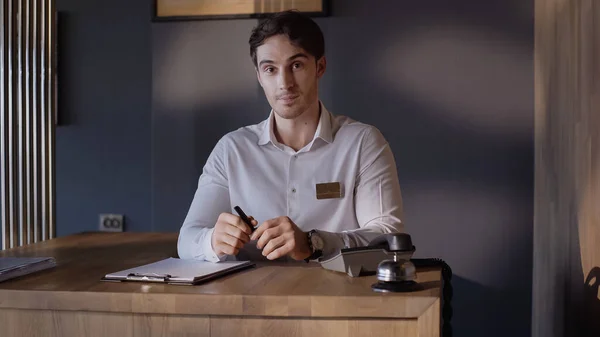 Joven recepcionista mirando a la cámara mientras está de pie en el mostrador de recepción - foto de stock