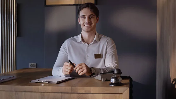 Feliz recepcionista mirando a la cámara mientras está de pie en el mostrador de recepción - foto de stock