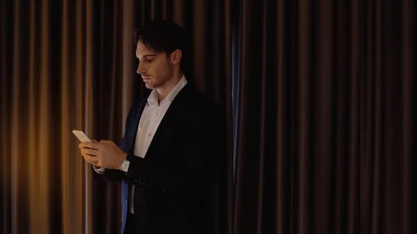 Hombre de negocios serio charlando en el teléfono inteligente en la habitación de hotel - foto de stock