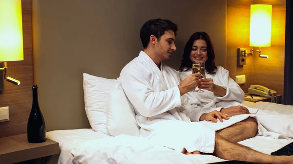 Heureux couple en peignoirs cliquetis verres avec champagne dans la chambre d'hôtel — Stock Photo