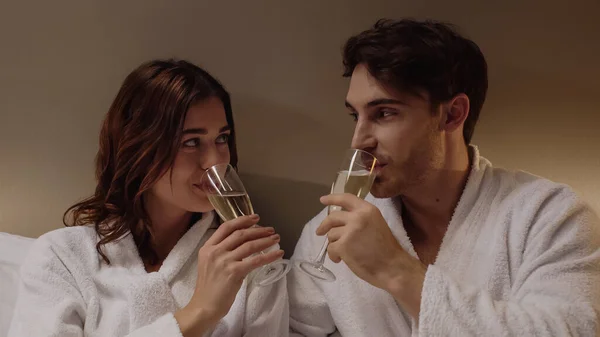 Щаслива пара в халатах п'є шампанське в готельному номері — стокове фото