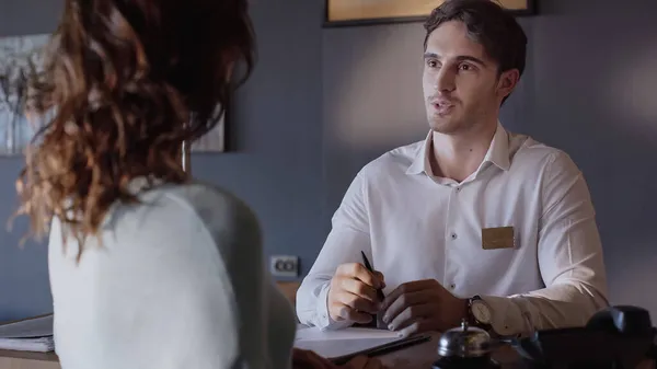 Young hotel receptionist talking with blurred client at hotel counter — Stock Photo