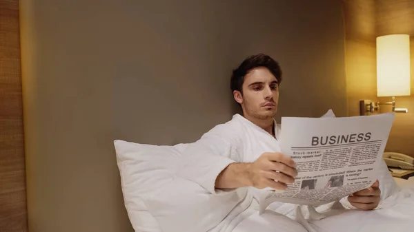 Homem focado lendo jornal de negócios no quarto de hotel — Fotografia de Stock