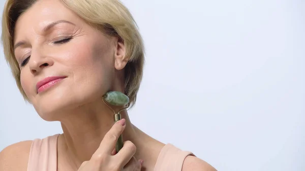 Middle aged woman massaging neck with jade roller isolated on white — Stock Photo