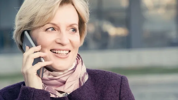 Felice donna di mezza età guardando lontano mentre parla su smartphone all'aperto — Foto stock