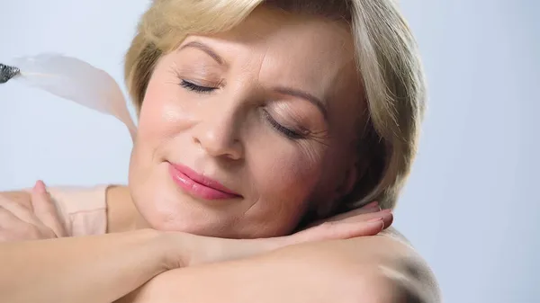 Close up view of middle aged woman with closed eyes smiling near feather isolated on white — Stock Photo