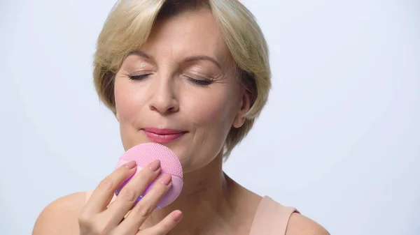 Donna di mezza età con occhi chiusi pulizia viso con detergente in silicone isolato su bianco — Foto stock