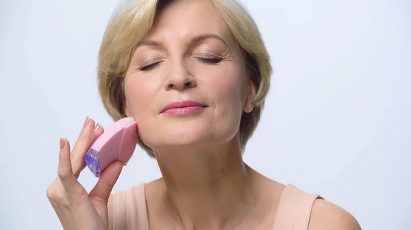 Donna matura ad occhi chiusi utilizzando detergente siliconico sul viso isolato su bianco — Foto stock