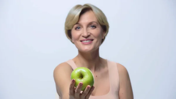 Sfocata donna di mezza età mostrando mela verde e sorridendo alla fotocamera isolata su bianco — Foto stock