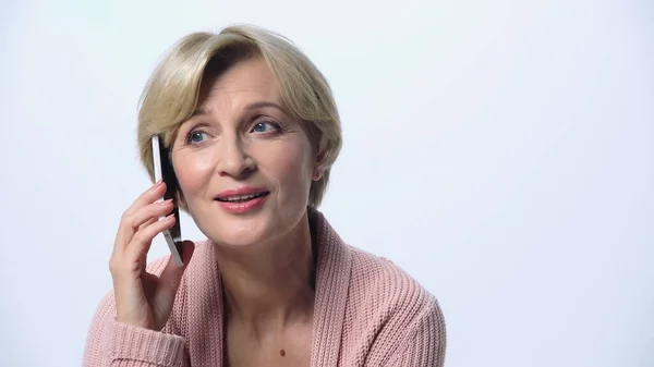 Mujer de mediana edad sonriendo durante la conversación en el teléfono inteligente aislado en blanco - foto de stock