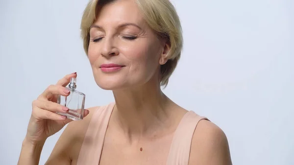 Mulher de meia idade com olhos fechados desfrutando odor de perfume isolado no branco — Fotografia de Stock