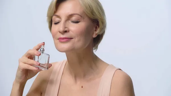 Mujer de mediana edad con los ojos cerrados disfrutando de olor de perfume aislado en blanco — Stock Photo