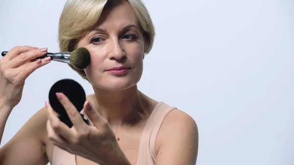 Blonde middle aged woman applying face powder isolated on white — Stock Photo