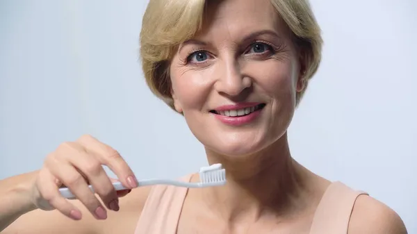 Sorridente donna di mezza età in possesso di spazzolino da denti con dentifricio isolato su bianco — Foto stock