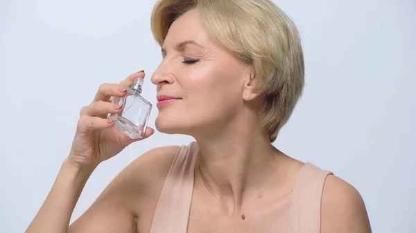 Mujer de mediana edad con los ojos cerrados disfrutando de olor de perfume aislado en blanco - foto de stock