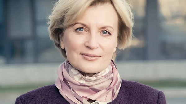 Positive middle aged woman in neck scarf looking at camera outdoors — Stock Photo