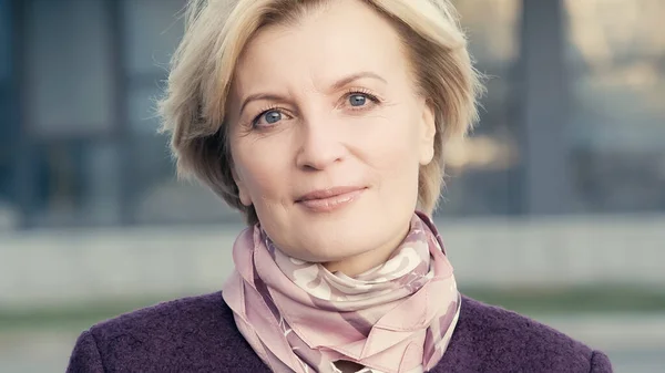 Blonde middle aged woman in elegant neckerchief looking at camera outdoors — Stock Photo