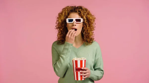 Нервова жінка в 3d окулярах дивиться фільм з попкорн відром ізольовано на рожевому — стокове фото
