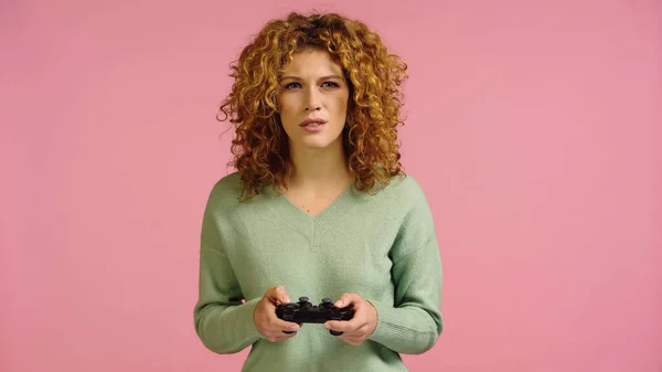 KIEW, UKRAINE - 22. DEZEMBER 2021: Konzentrierte rothaarige Frau spielt Videospiel isoliert auf rosa — Stockfoto