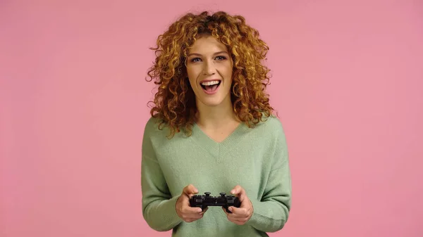 KYIV, UKRAINE - DECEMBER 22, 2021: excited redhead woman gaming isolated on pink — Stockfoto