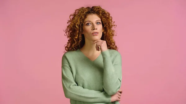 Donna sorpresa con i capelli ricci che si tengono per mano vicino al viso e guardando la fotocamera isolata sul rosa — Foto stock