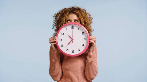 Tricky woman obscuring face with round clock while looking aside isolated on blue — Stock Photo