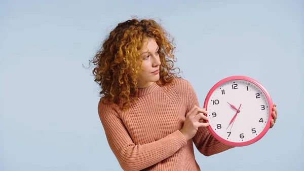 Mujer pelirroja sorprendida mirando reloj redondo aislado en azul - foto de stock