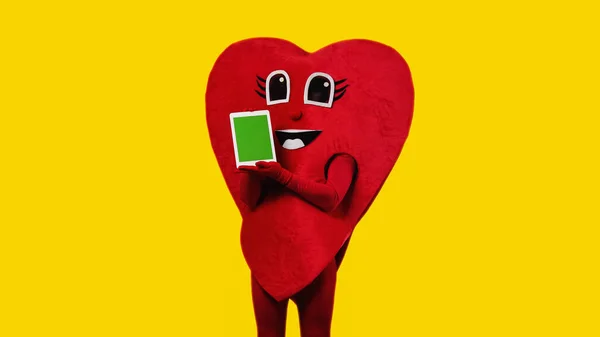 Persona en traje de corazón rojo celebración tableta digital con pantalla verde aislado en amarillo - foto de stock