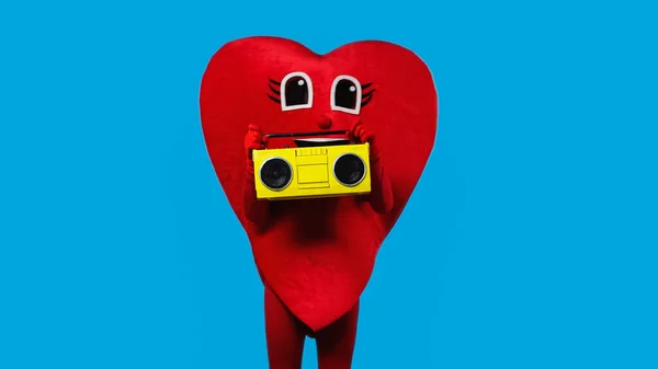 Persona in costume cuore rosso con contenitore retrò boombox isolato su blu — Foto stock