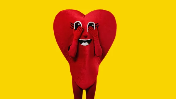 Persona in costume cuore toccando gli occhi dei cartoni animati isolati su giallo — Foto stock