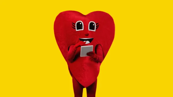 Persona en traje de corazón rojo sosteniendo tableta digital aislada en amarillo - foto de stock