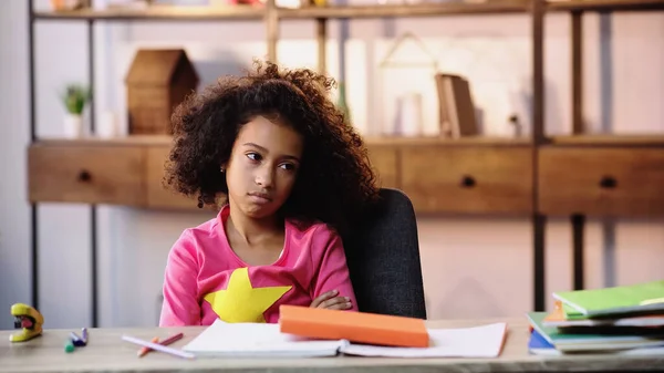 Displeased african american child looking away while doing homework — Fotografia de Stock