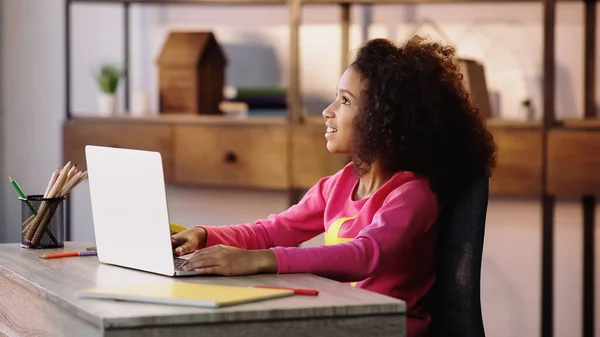 Criança americana africana satisfeito olhando para longe perto do laptop — Fotografia de Stock