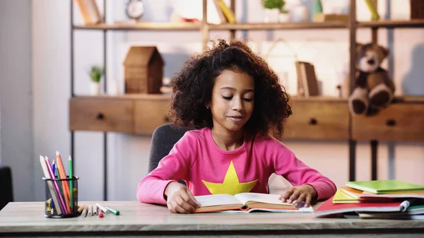 Lächelnd afrikanisches amerikanisches Kind liest Buch zu Hause — Stockfoto