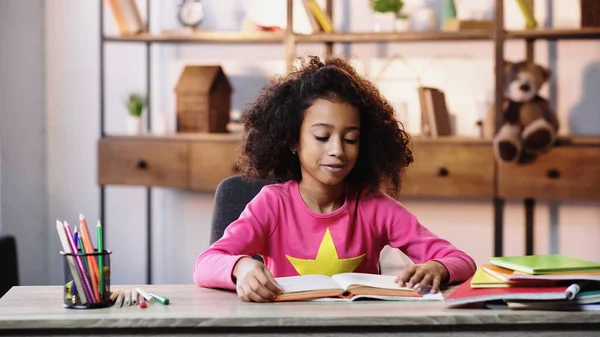 Smiling african american child reading book at home — Stock Photo