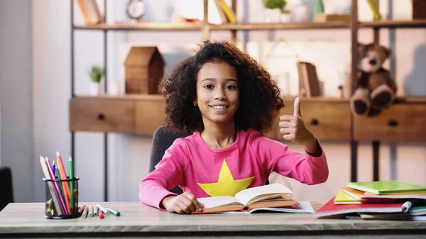 Sorrindo afro-americano criança leitura livro e mostrando polegar para cima — Fotografia de Stock