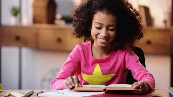 Feliz menina afro-americana ler livro em casa — Fotografia de Stock