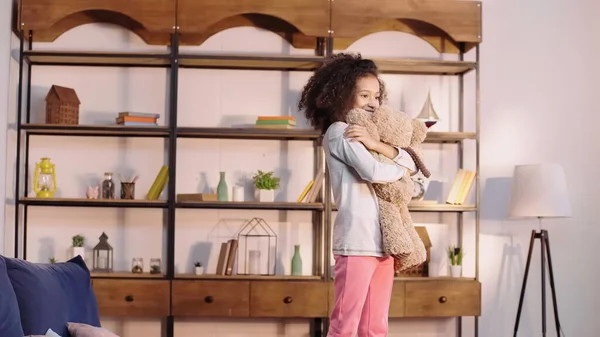 Happy african american girl hugging teddy bear in living room — Fotografia de Stock