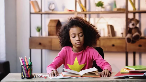 Encaracolado afro-americano criança leitura livro em casa — Fotografia de Stock