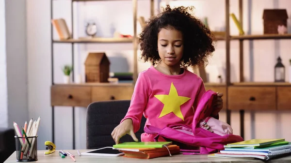 Sac à dos d'emballage enfant afro-américain frisé près de la tablette numérique sur la table — Photo de stock