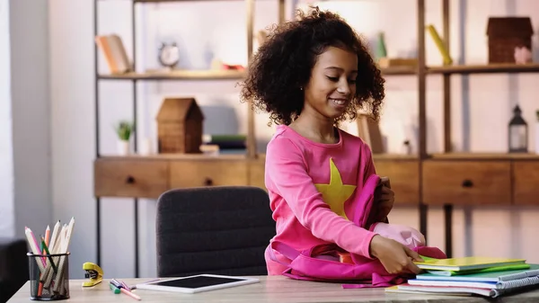 Happy african american child packing notebooks in backpack — Stockfoto