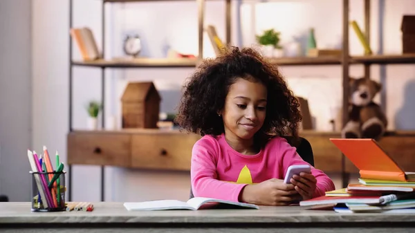 Niño afroamericano sonriente usando teléfono móvil cerca de portátiles - foto de stock