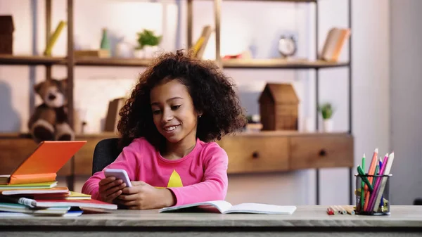 Cheerful african american child using mobile phone near notebooks — Stock Photo