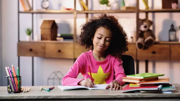 Menina afro-americana feliz escrevendo em notebook em casa — Fotografia de Stock