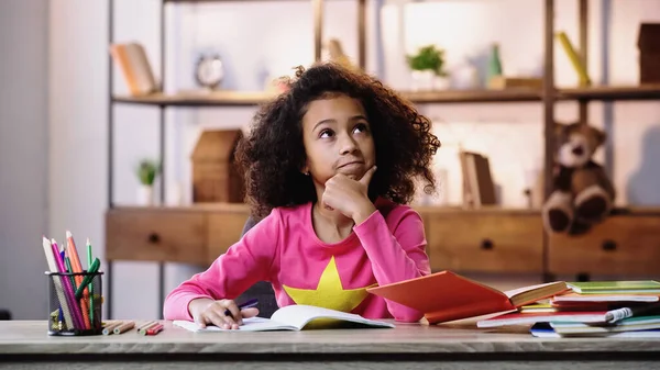 Thoughtful african american schoolgirl doing homework — Stock Photo